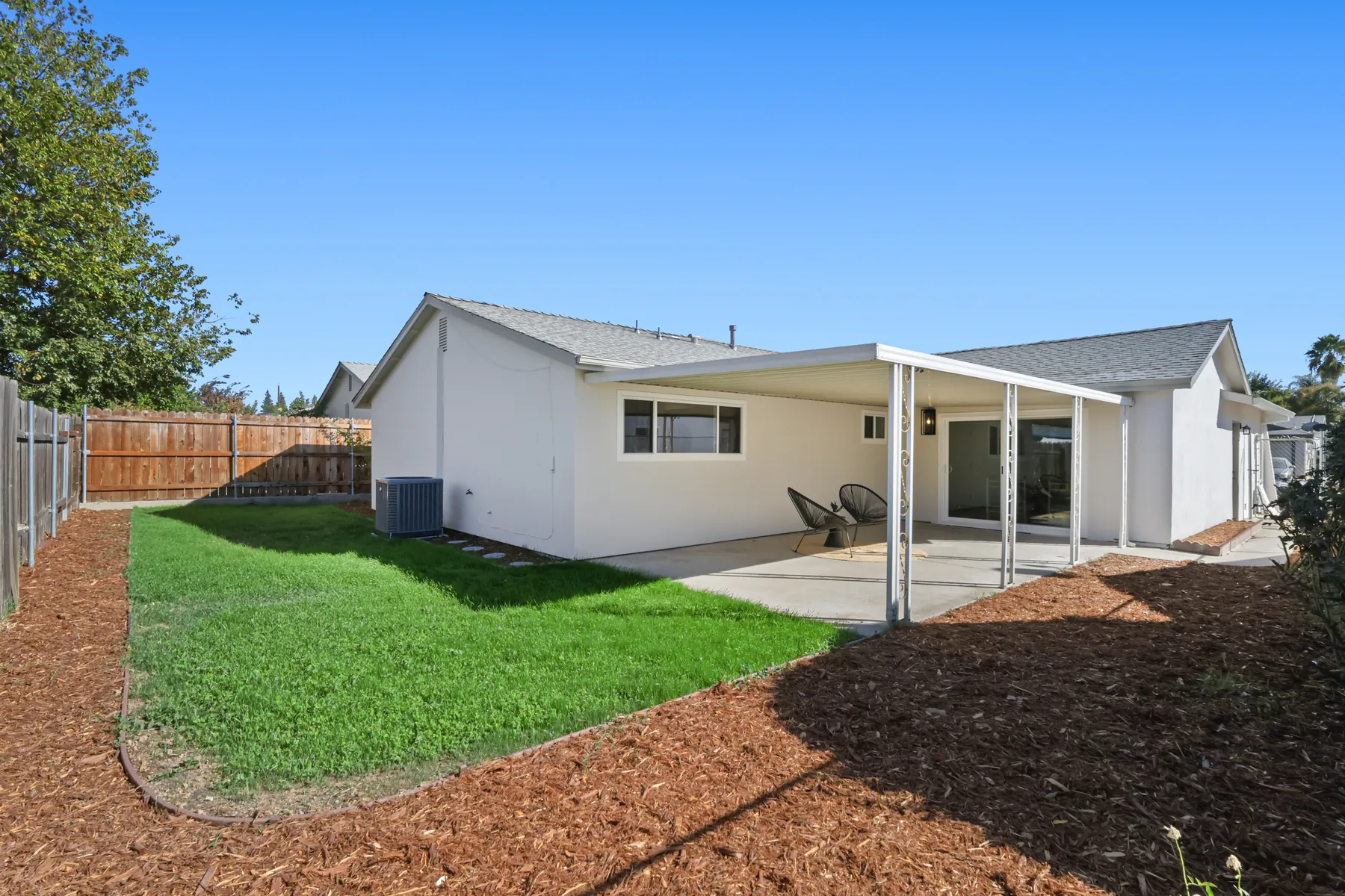 The rear yard with a new lawn and mulched beds along the fence line, and the rear elevation finished in the same white stucco as the front.
