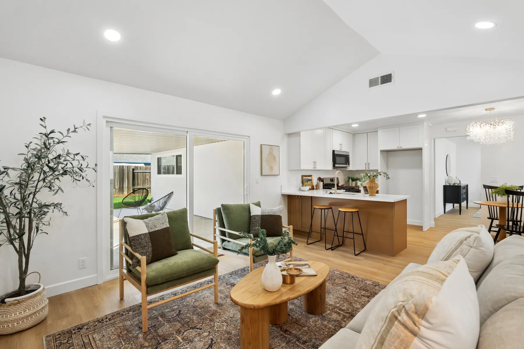 The living area opening to the kitchen under a vaulted ceiling, with recessed lighting and wood-look plank flooring.