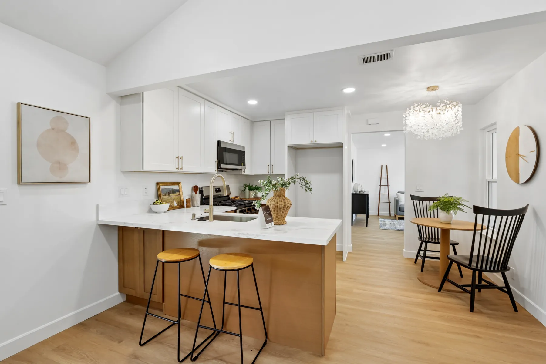 Kitchen peninsula with white shaker-style upper cabinets, wood-tone base cabinets, a quartz-look counter and a gold-finish faucet.