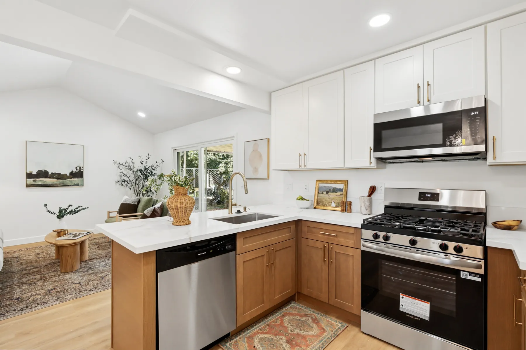 The kitchen's cooking wall: white shaker-style uppers over wood-tone lowers, with stainless appliances and gold-finish hardware.