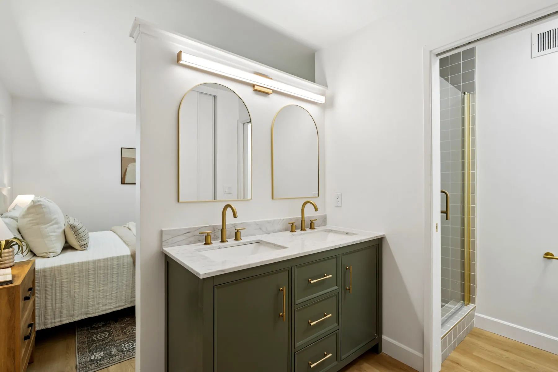 Bathroom with a double vanity in a dark green finish, a light stone-look top, arched mirrors and gold-finish fixtures.