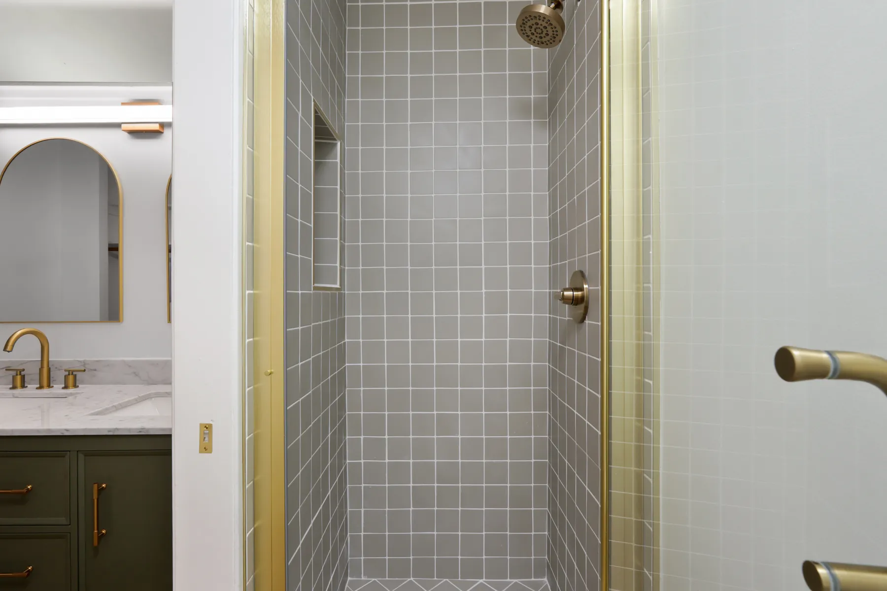 Shower tiled in grey square tile, with a recessed niche and gold-finish trim.